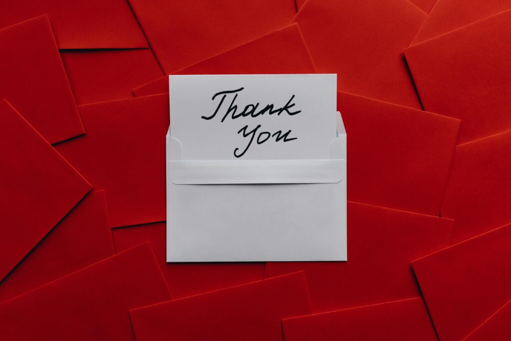 Elegant thank you card in white envelope on vibrant red envelopes flatlay. Perfect for gratitude themes.